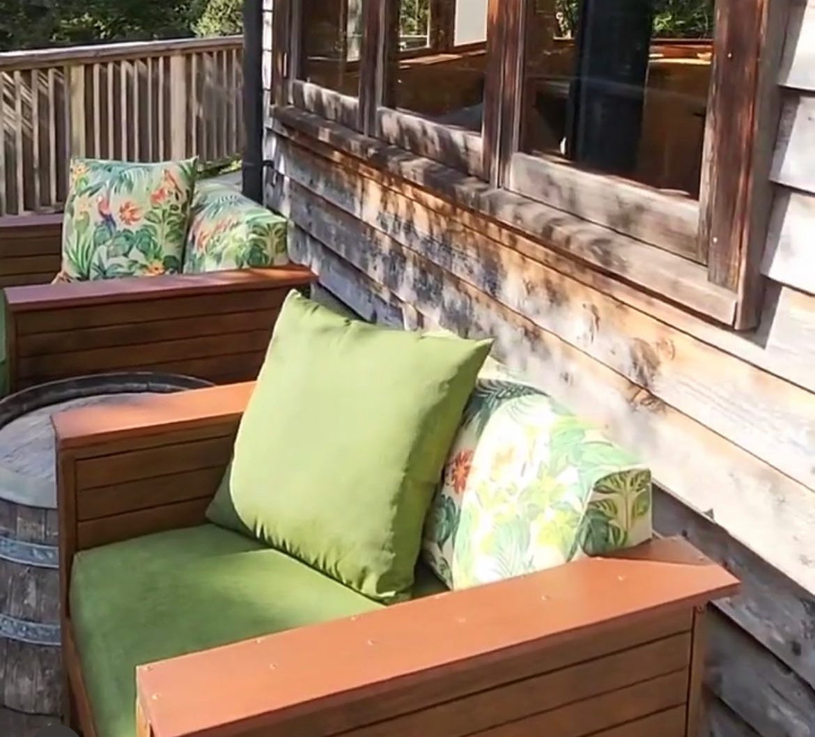 Wooden outdoor seating area with green cushions and floral-patterned pillows on a wooden deck.